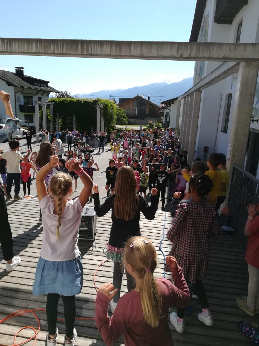 Lehrpersonen und Kinder tanzend und singend am Schulhof