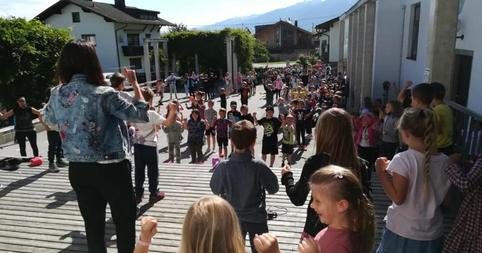 Lehrpersonen und Kinder am Schulhof - singend und tanzend